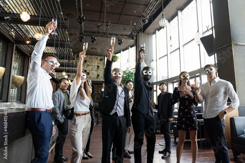 Group of diverse business people wear fantasy face mask and holding glasses of champagne for celebration in his company