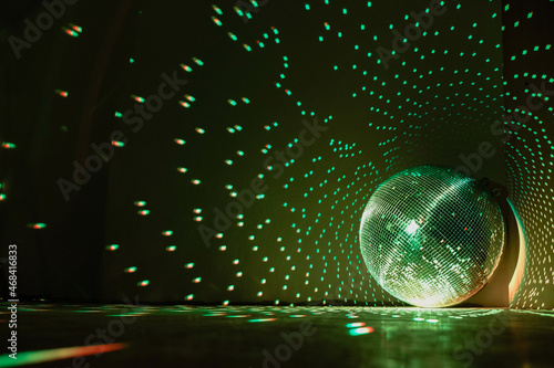 Fototapeta Large disco ball reflecting green light in a dark hall for discos