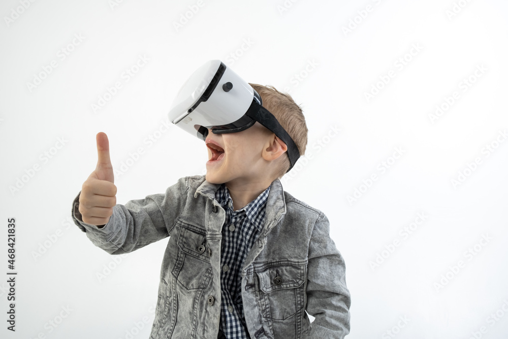 Young boy with virtual reality glasses isolated on white background holds approving hand gesture. A child in emotional excitement wearing 3D glasses. Young boy with virtual reality glasses isolated on white background holds approving hand gesture. A child in emotional excitement wearing 3D glasses.