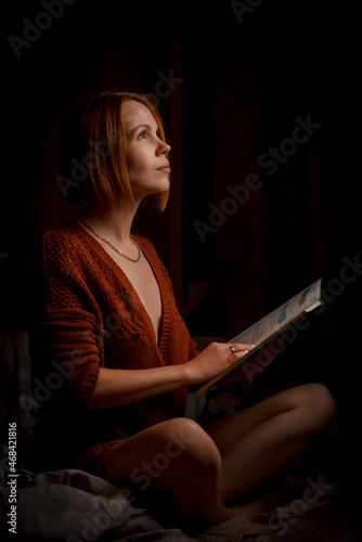 A woman is holding a book and thinking in the dark.