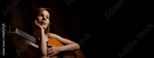Sensual attractive woman holding an acoustic guitar on a black background. Banner. Place for your text.