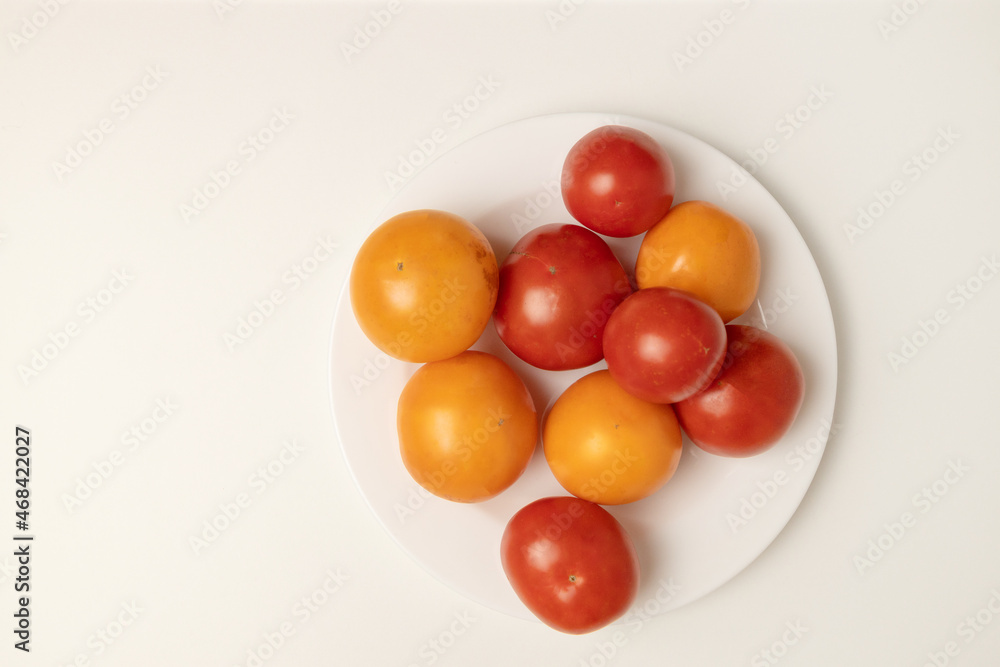 Healthy food composition of various fresh yellow and red tomato isolated on a white plate on grey background.