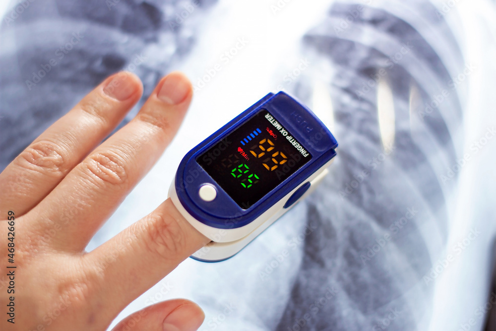 Woman hand with medical fingertip pulse oximeter tool for oxygen saturation check during covid virus desease. SpO2 monitoring and heart rate measurement instrument with x-ray of chest scan. Woman hand with medical fingertip pulse oximeter tool for oxygen saturation check during covid virus desease. SpO2 monitoring and heart rate measurement instrument with x-ray of chest scan.