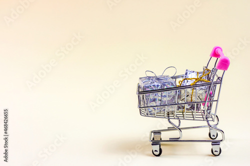Trolley shopping cart with silver Xmas and Birthday boxes for gifts and presents on light background with copy space. Christmas sale, Black Friday and Cyber Monday discounts, holiday shopping concept.