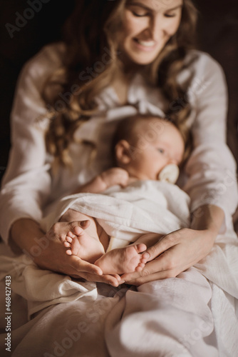 Beautiful young mother holds newborn baby girl in white lighter room at home. Tenderness cozy atmosphere