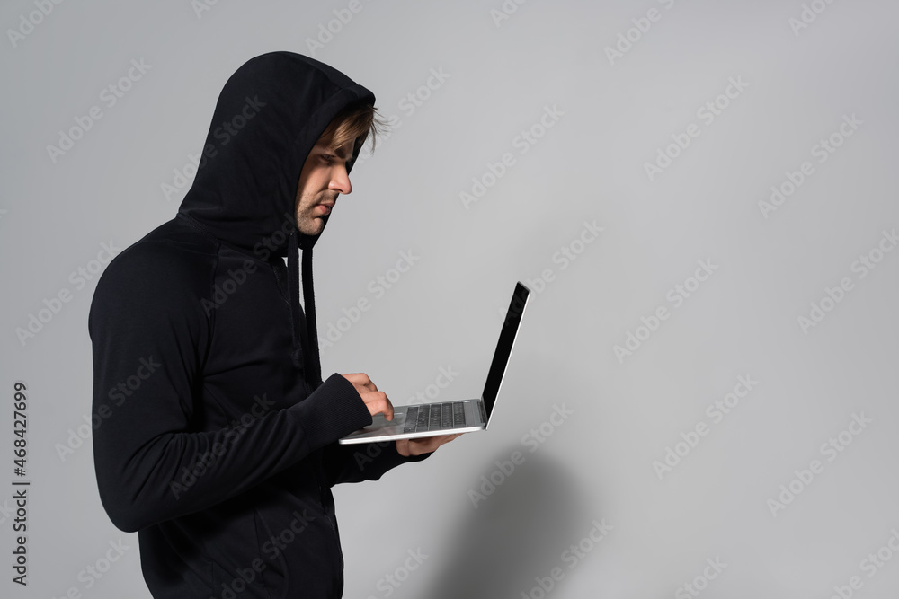 Side view of hacker using laptop on grey background Side view of hacker using laptop on grey background