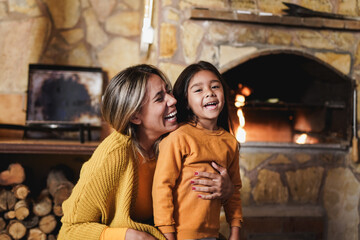 Mother hugging little daughter near fireplace at home during winter time - Mother and child love