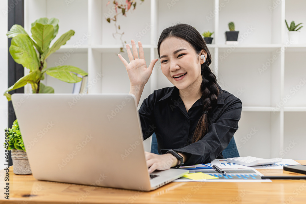 Conceptual Asian businesswoman is video calling with coworker, she is greeting people in chat, she greets with friendly smile, she looks at laptop to chat with friend. Using technology to communicate. Conceptual Asian businesswoman is video calling with coworker, she is greeting people in chat, she greets with friendly smile, she looks at laptop to chat with friend. Using technology to communicate.