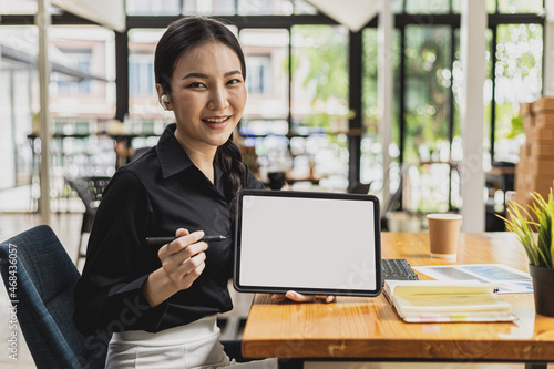 A beautiful Asian woman with a smiling face, she is a coffee shop owner, holding a tablet with a blank screen white background for inserting text or advertisements. copy space.