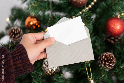 Hand holding mockup christmas greeting card for invitation design on christmas tree background. photo