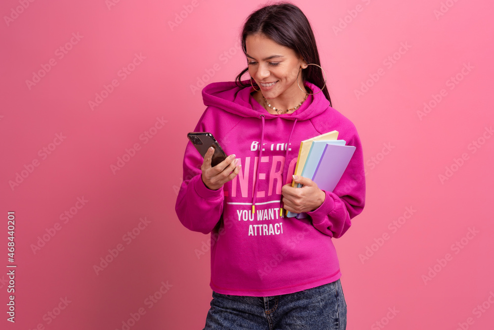 hispanic pretty woman in pink hoodie smiling holding holding notebooks and using smartphone hispanic pretty woman in pink hoodie smiling holding holding notebooks and using smartphone