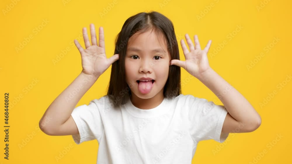 Funny Little Korean Girl Sticking Out Tongue Grimacing, Yellow Background Funny Little Korean Girl Sticking Out Tongue Grimacing, Yellow Background