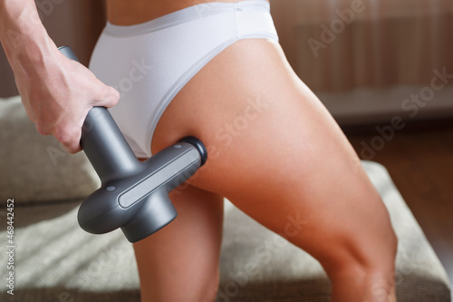 Self-massage of the female buttock with a percussion massage gun at home.