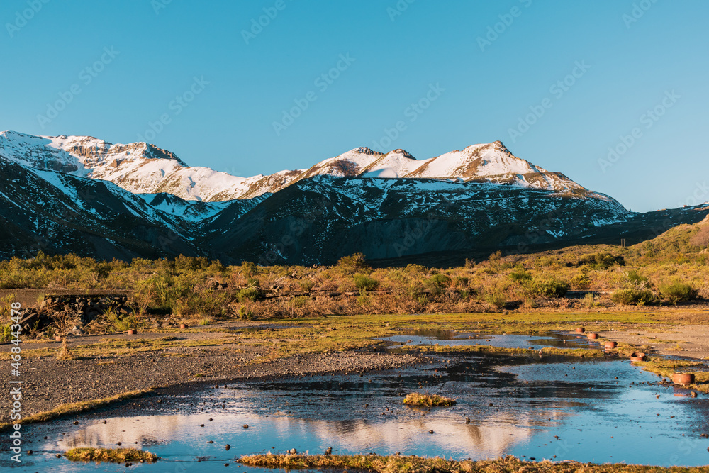 montañas nevadas reflejos en el agua , hora dorada al atardecer, coloreas azul y verdes 