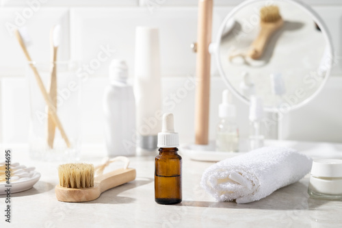 Massage oil or facial serum in a glass bottle in the bathroom. White towel, cream, toothbrushes in the background.