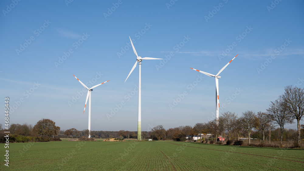 Three red and white wind turbines for power generation in Germany with a blue sky in the background and a green field in the foreground Three red and white wind turbines for power generation in Germany with a blue sky in the background and a green field in the foreground
