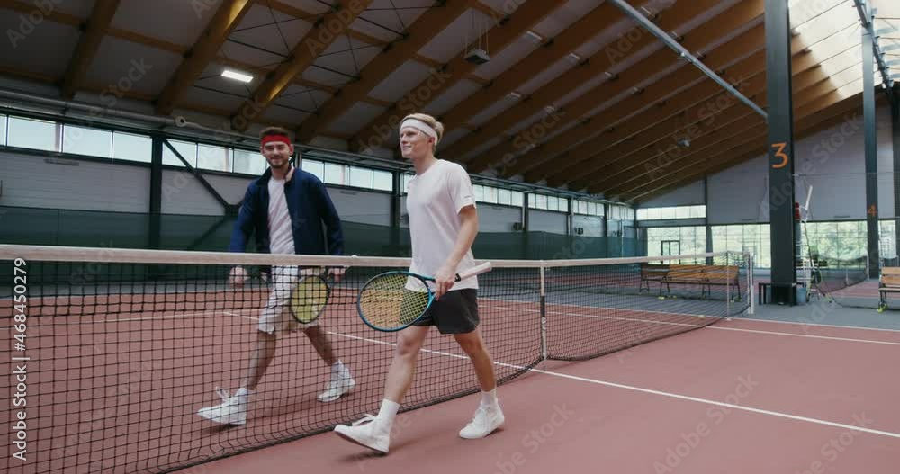 Two men greet each other, shaking hands across the net about to play tennis Two men greet each other, shaking hands across the net about to play tennis