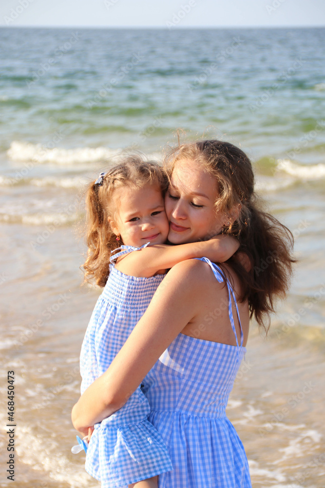 The concept of a happy harmonious family and happy motherhood outdoors. Mother hugs her baby against the background of the sea The concept of a happy harmonious family and happy motherhood outdoors. Mother hugs her baby against the background of the sea