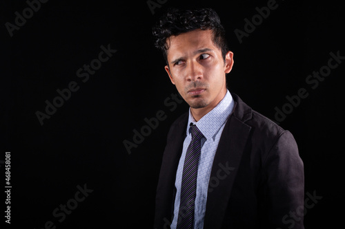 Businessman suspicious of something he looks askance at. Young latin with suspicious look and expression, looking for something. Isolated on a black background. photo