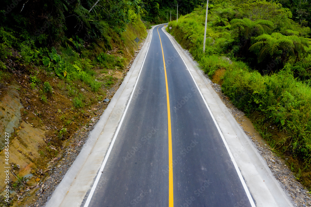A hardened road divided with a yellow line running down a mountain slope A hardened road divided with a yellow line running down a mountain slope