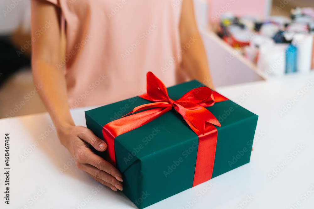 Close-up of unrecognizable female hands holding wrapped Christmas gift box tied red ribbon and decorated beautiful bow, closeup. Xmas or New year gift in stylish wrapping paper with red ribbon. Close-up of unrecognizable female hands holding wrapped Christmas gift box tied red ribbon and decorated beautiful bow, closeup. Xmas or New year gift in stylish wrapping paper with red ribbon.