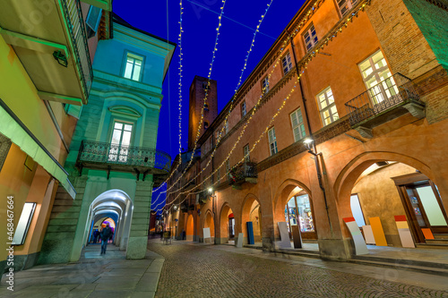 Cobblestone street and historic buildings illuminated by Christmas lights in Alba  Italy.