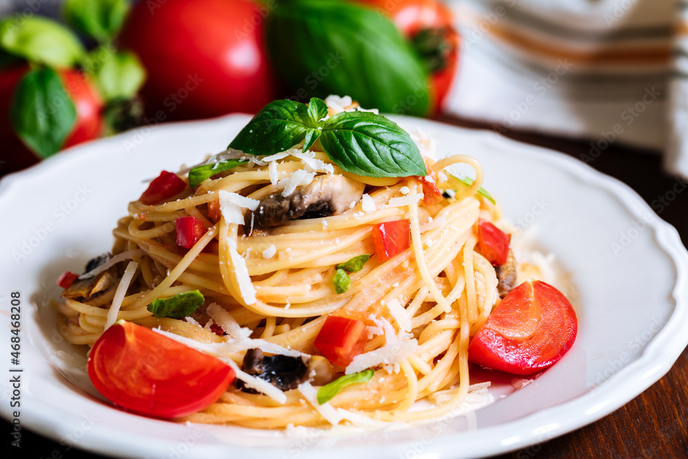 Fresh pasta with spaghetti, tomato, mushrooms, basil and parmesan cheese in white plate on a wooden background with ingredients in background Fresh pasta with spaghetti, tomato, mushrooms, basil and parmesan cheese in white plate on a wooden background with ingredients in background