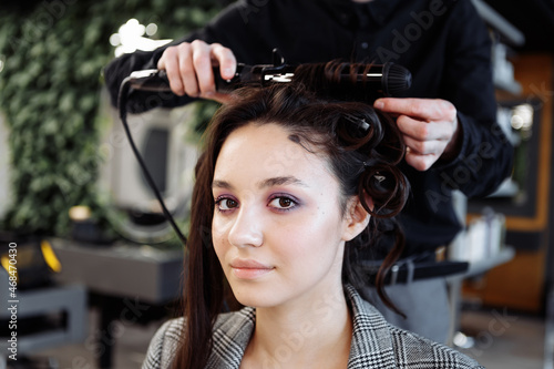 The master does hair styling in a beauty salon. Young woman preparing for a date.