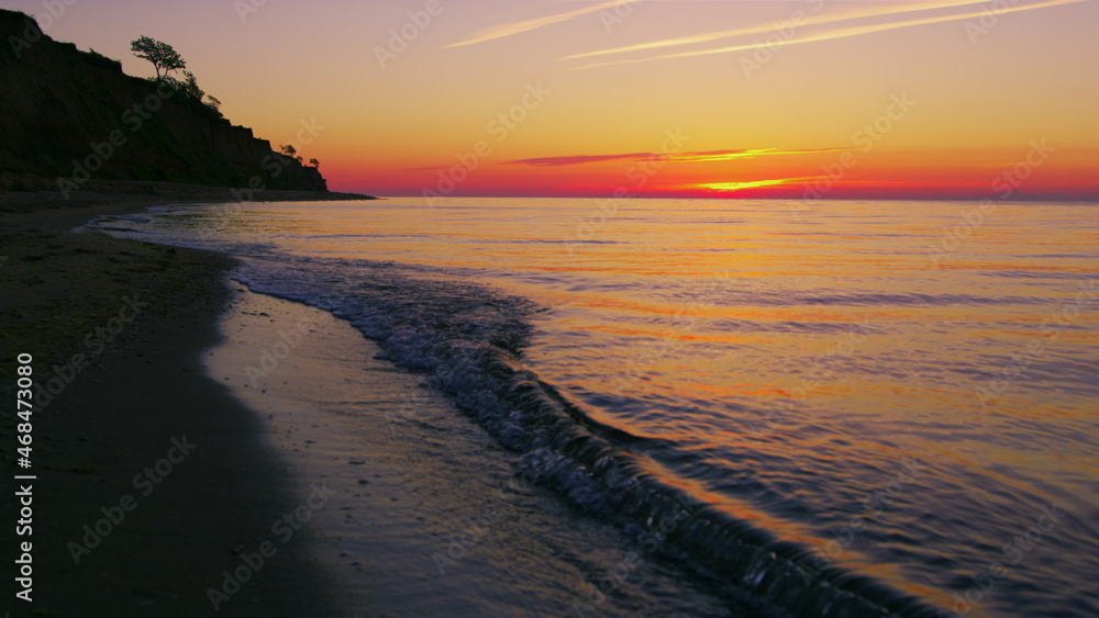 Beautiful view of rocky seashore against bright orange sunset in evening.