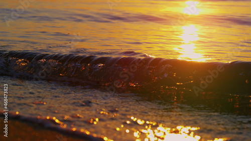 Closeup sea waves splashing beach sand at golden morning sunrise. Sun light