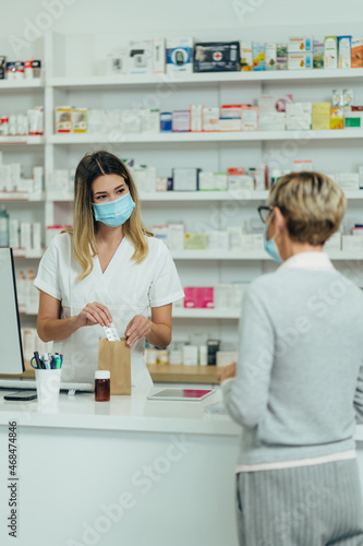 Pharmacist wearing protective mask and serving a customer patient in a pharmacy