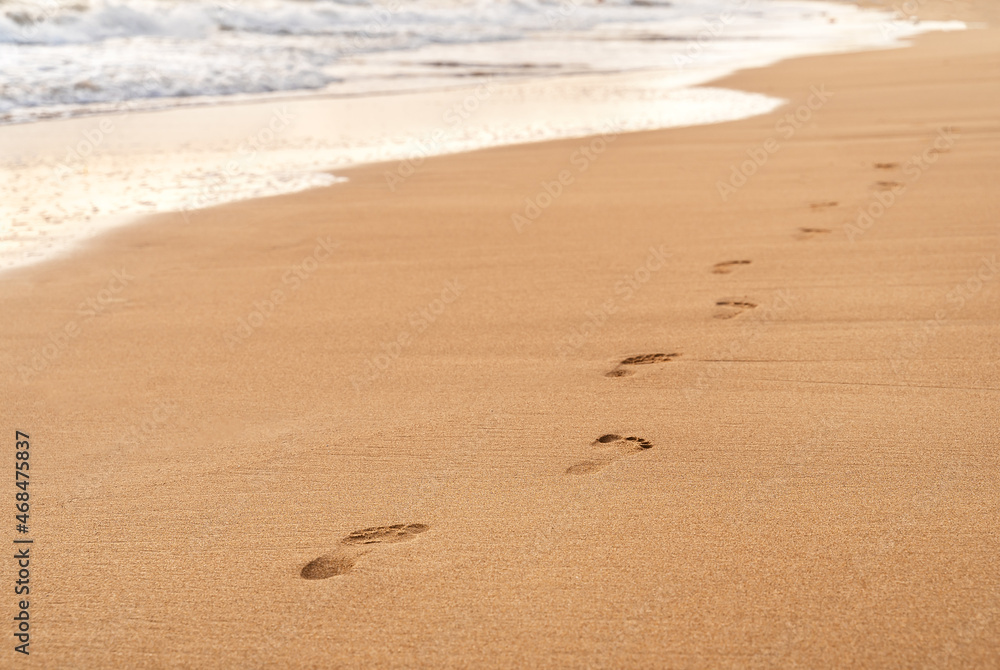 Footprints on the white sand of the beach along the wave. Summer vacation concept. Background for your design witn copy space. Footprints on the white sand of the beach along the wave. Summer vacation concept. Background for your design witn copy space.