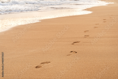 Footprints on the white sand of the beach along the wave. Summer vacation concept. Background for your design witn copy space.