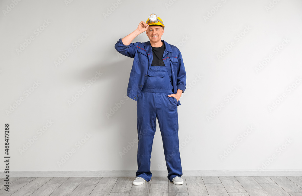Mature worker with headlamp flashlight near light wall Mature worker with headlamp flashlight near light wall