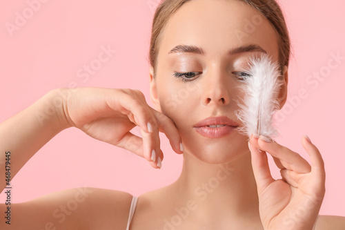 Beautiful young woman with soft feather on color background photo