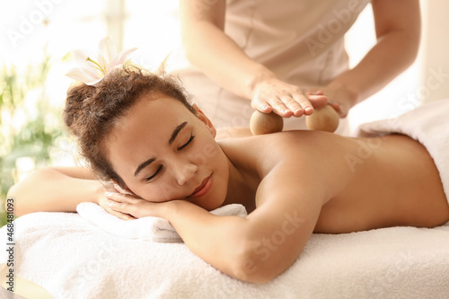 Young African-American woman getting massage with balls by therapist in spa salon