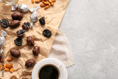 Tasty prunes, chocolate candies, almond nuts and cup of coffee on light table