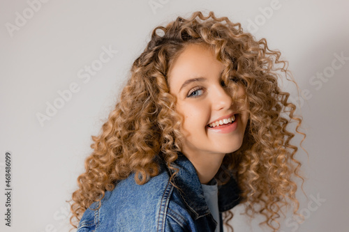 portrait of a cute smiling blonde girl with blue eyes and curly hair in a denim jacket. young woman with beautiful clean healthy skin. natural make up, spa concept, fashion concept. High quality photo