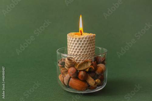 Burning candle in holder with autumn decor on color background