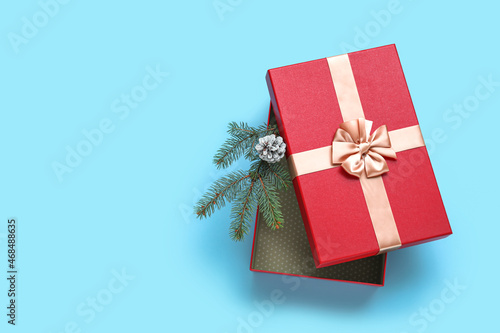Fototapeta Naklejka Na Ścianę i Meble -  Opened Christmas gift box with fir tree branch and pine cone on color background