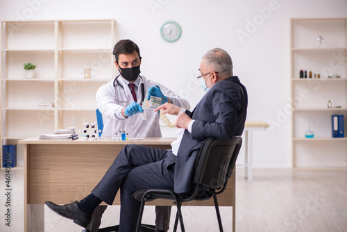Old businessman visiting young male doctor in vaccination concep