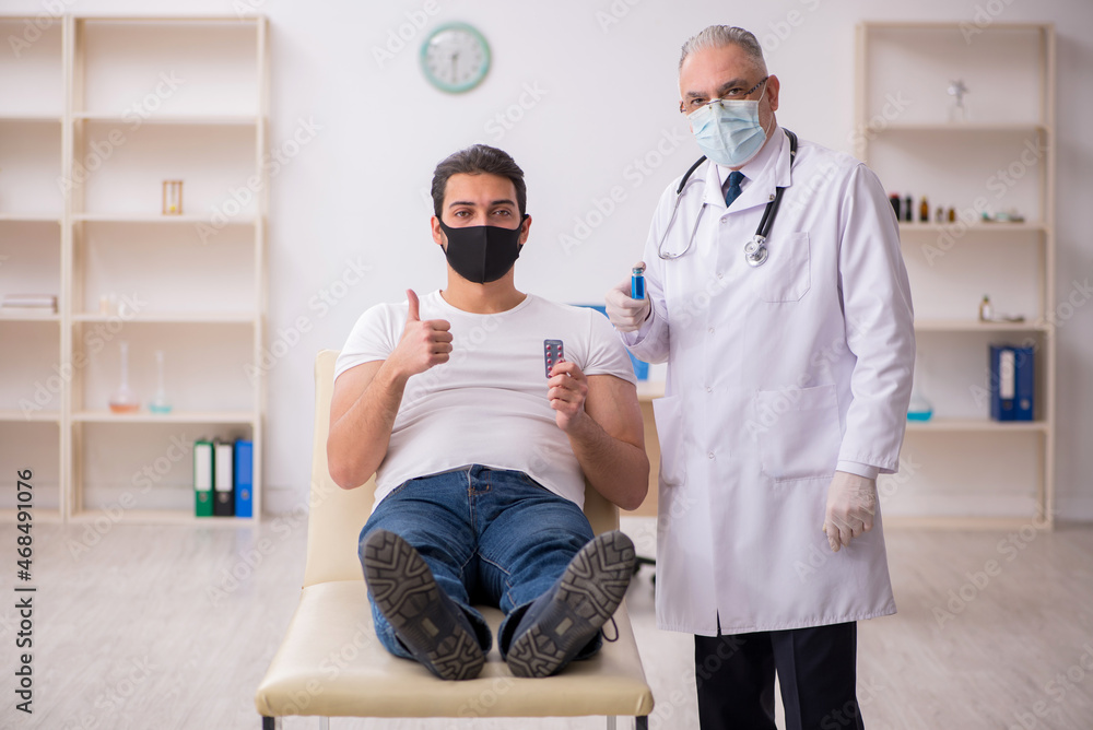 Fototapeta premium Young male patient visiting old doctor in vaccination concept