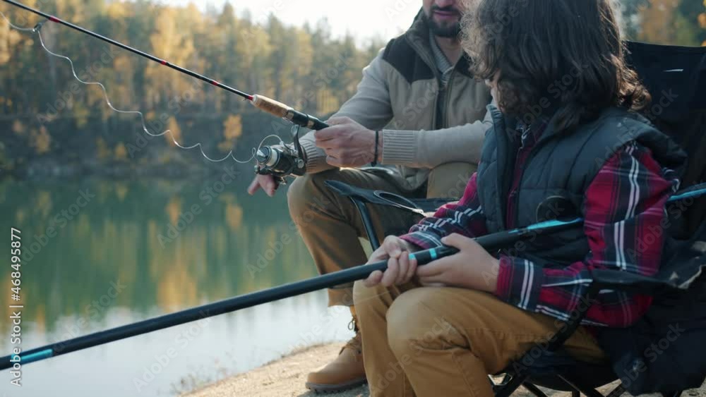 Caring father is teaching little boy talking and fishing in lake on beautiful autumn day. Outdoor adventures and family activities concept. Caring father is teaching little boy talking and fishing in lake on beautiful autumn day. Outdoor adventures and family activities concept.