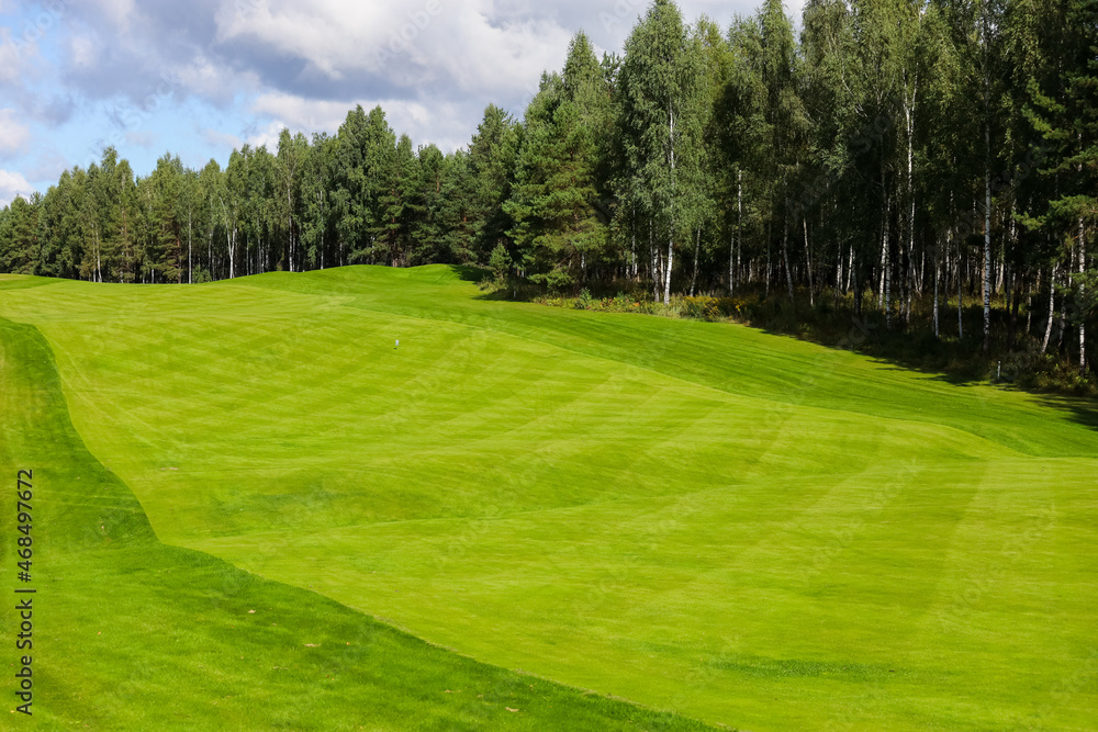 Golf course, landscape, green grass on the background of the forest and a bright sky with clouds. High quality photo