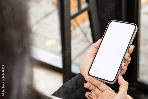 Top view mockup of a woman holding a black cell phone with the blank white screen while sitting at work for texting with space for tech marketing business ads