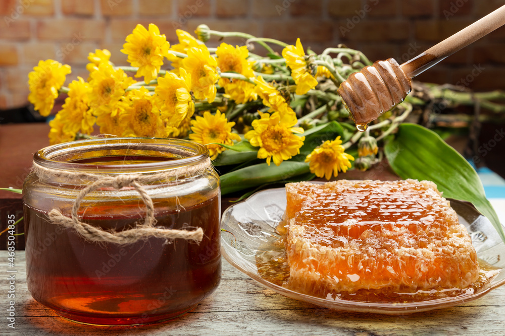 honeycomb with honey placed in a plate, a wooden dipper, a jar of honey, a yellow gerbera flower. put on old wooden planks honeycomb with honey placed in a plate, a wooden dipper, a jar of honey, a yellow gerbera flower. put on old wooden planks