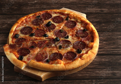 pepperoni pizza with sausage and olives on a dark wooden background