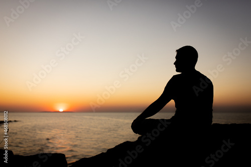 A man enjoys the view of the sunset on the sea, sitting on a rock. Side view, silhouette.