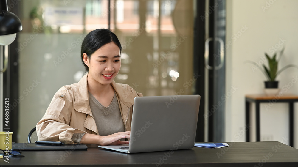 © Prathankarnpap - Smiling female graphic designer  working with laptop computer at office desk.