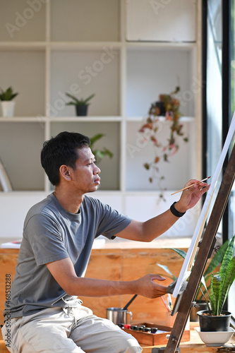 Side view of young asian man painting on canvas in art studio.